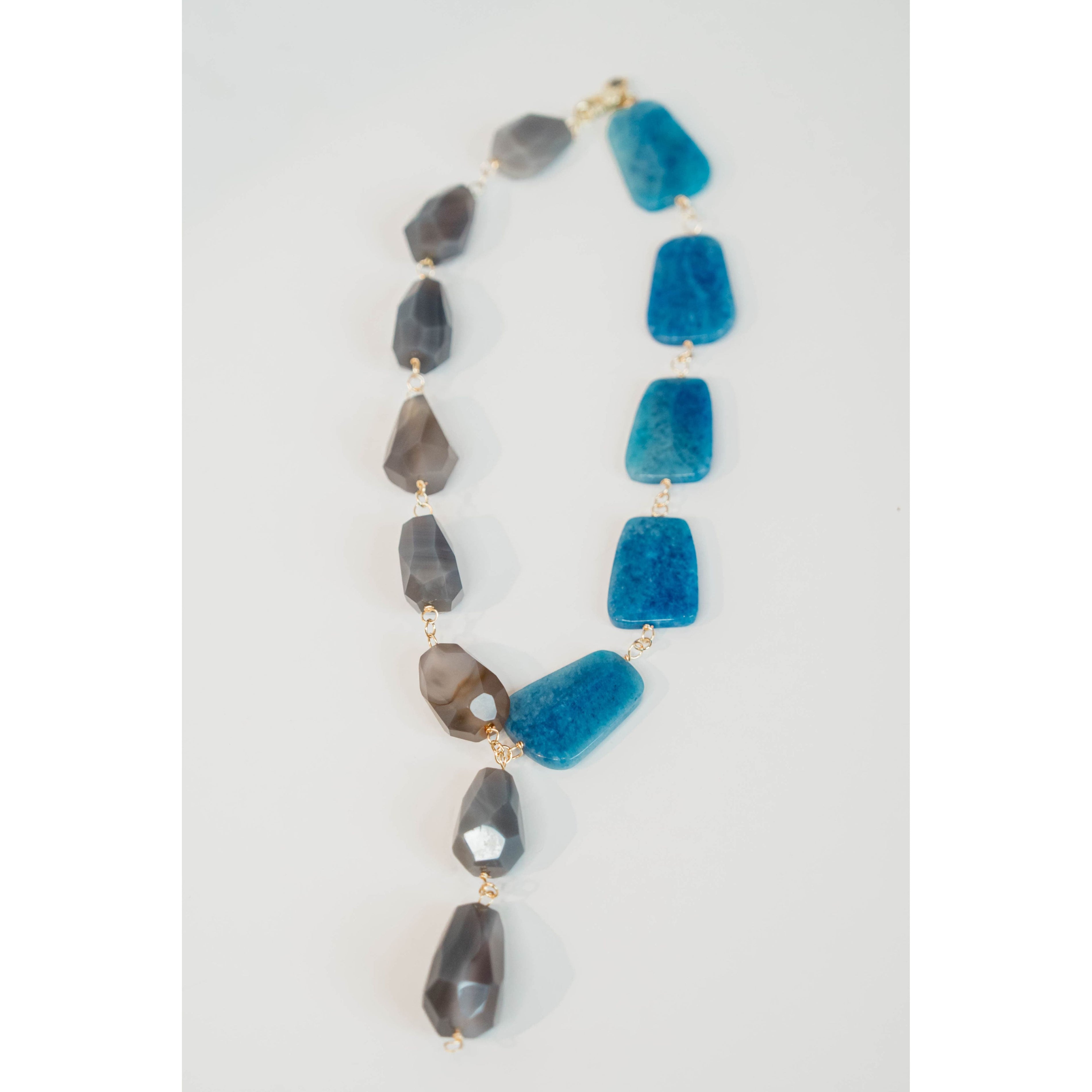statement necklace with gold chain and blue and grey stone accents on a light grey background