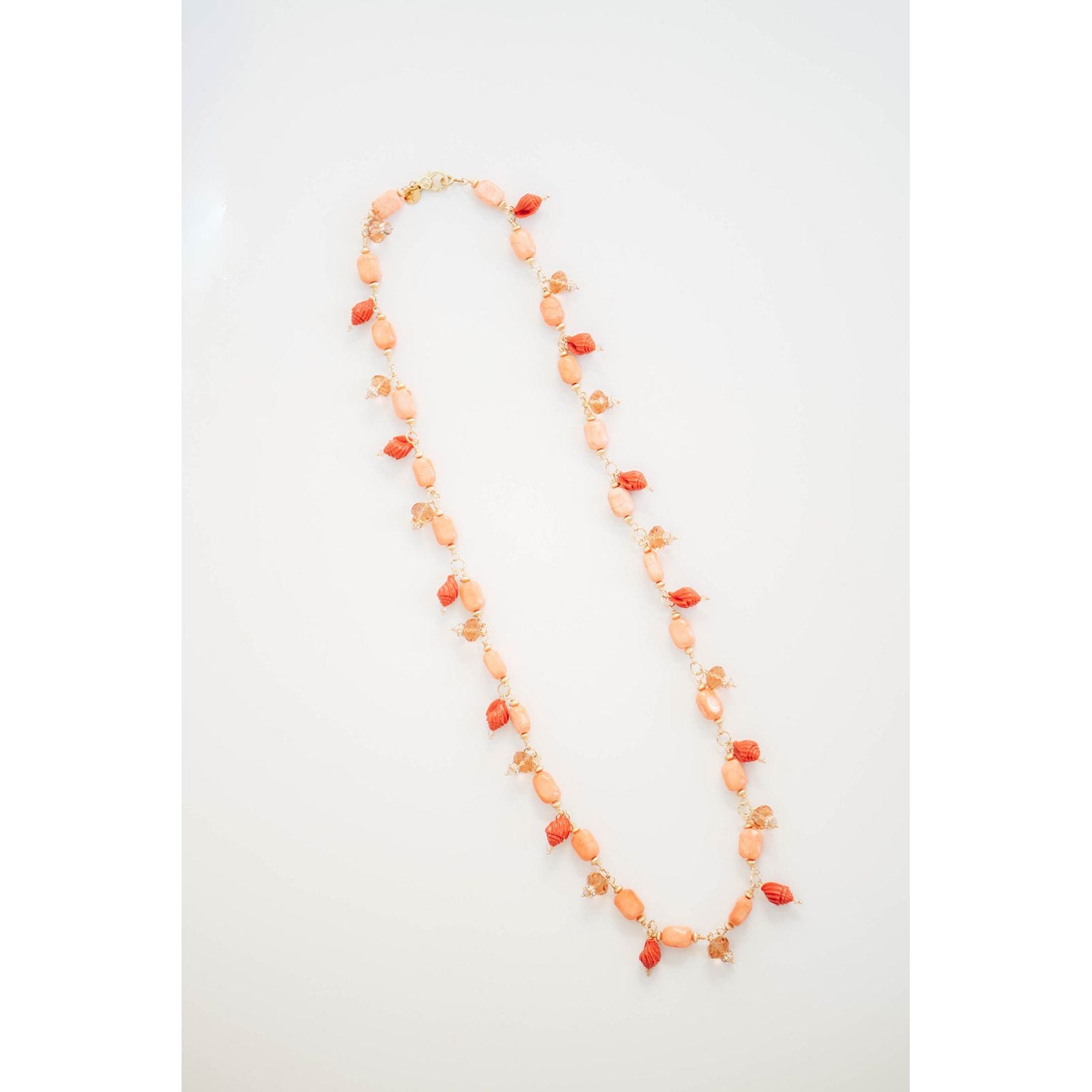 Faceted crystal beads and conch shell shaped beads are dangling off a long orange beaded chain necklace