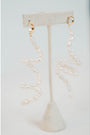 flexible pearl drop earrings with gold huggie posts on a neutral earring stand against a light gray background