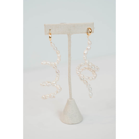 flexible pearl drop earrings with gold huggie posts on a neutral earring stand against a light gray background