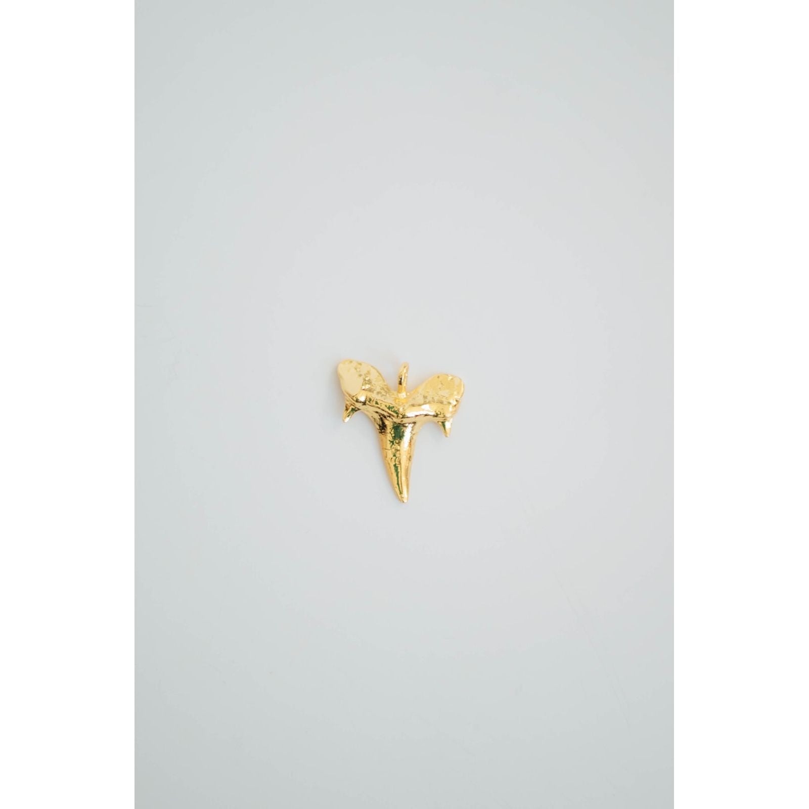 Gold textured shark tooth charm on a light gray background