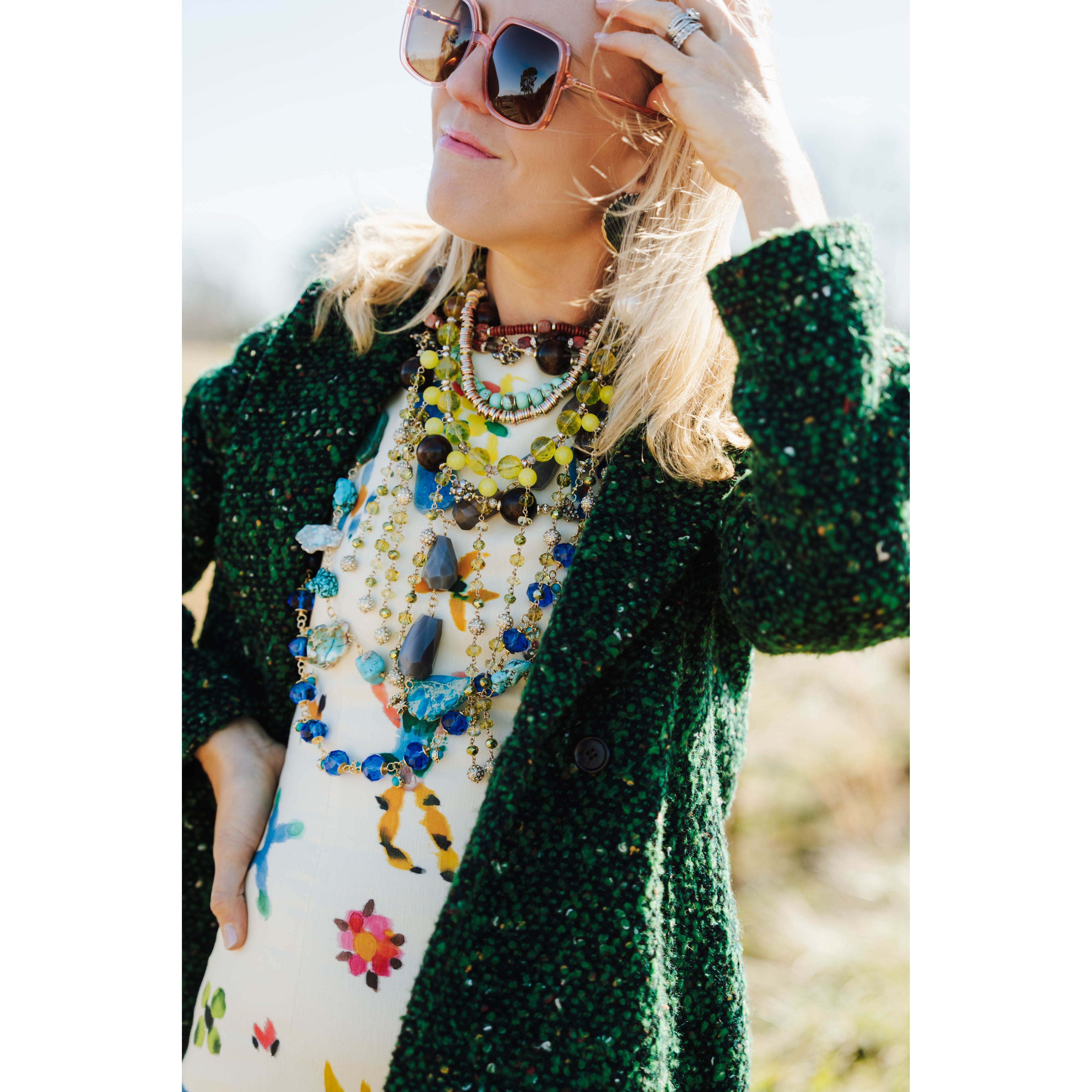 woman wearing a colorful outfit and various colorful necklaces with a blurred outdoor background