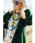 woman wearing a colorful outfit and various colorful necklaces with a blurred outdoor background