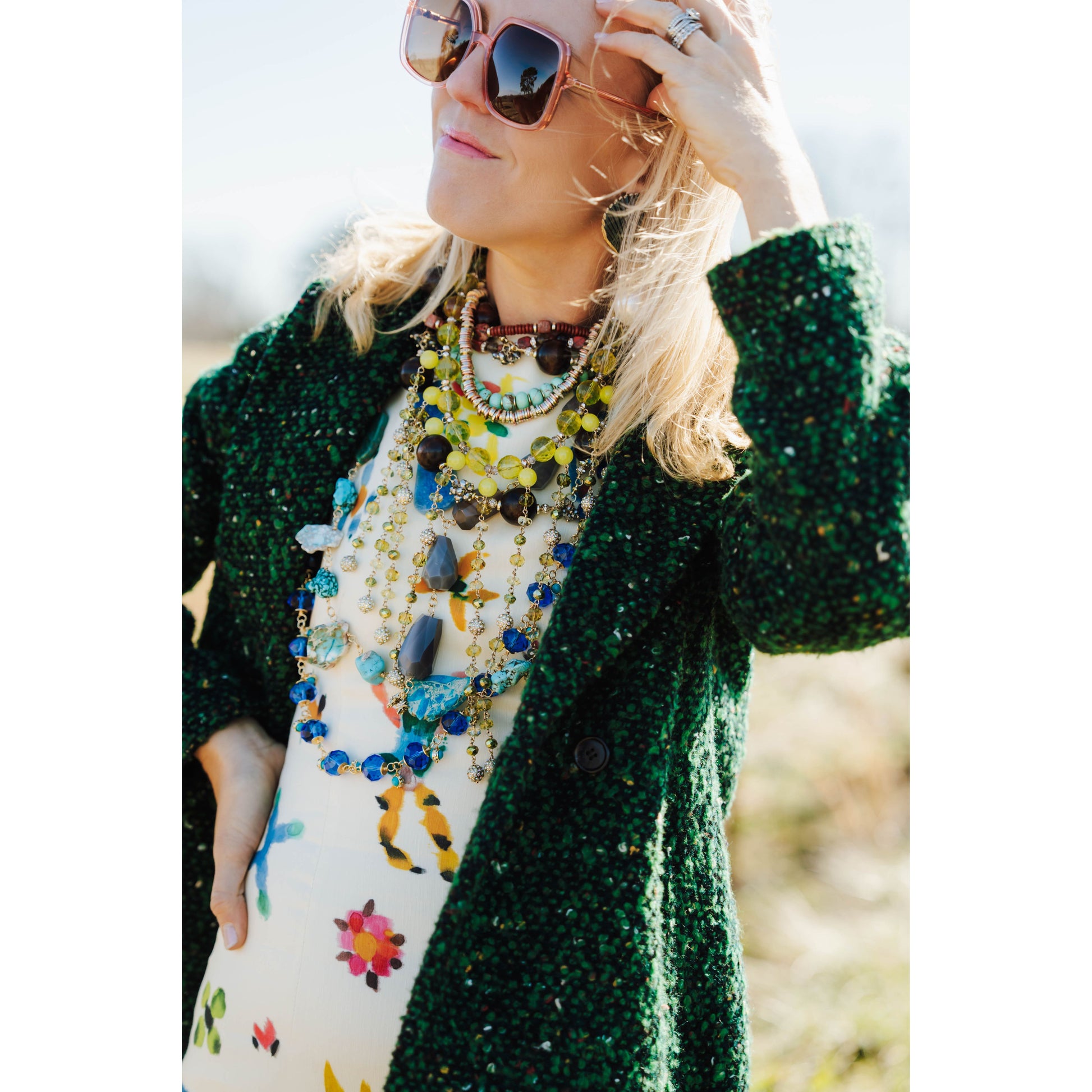 woman wearing a colorful outfit and various colorful necklaces with a blurred outdoor background
