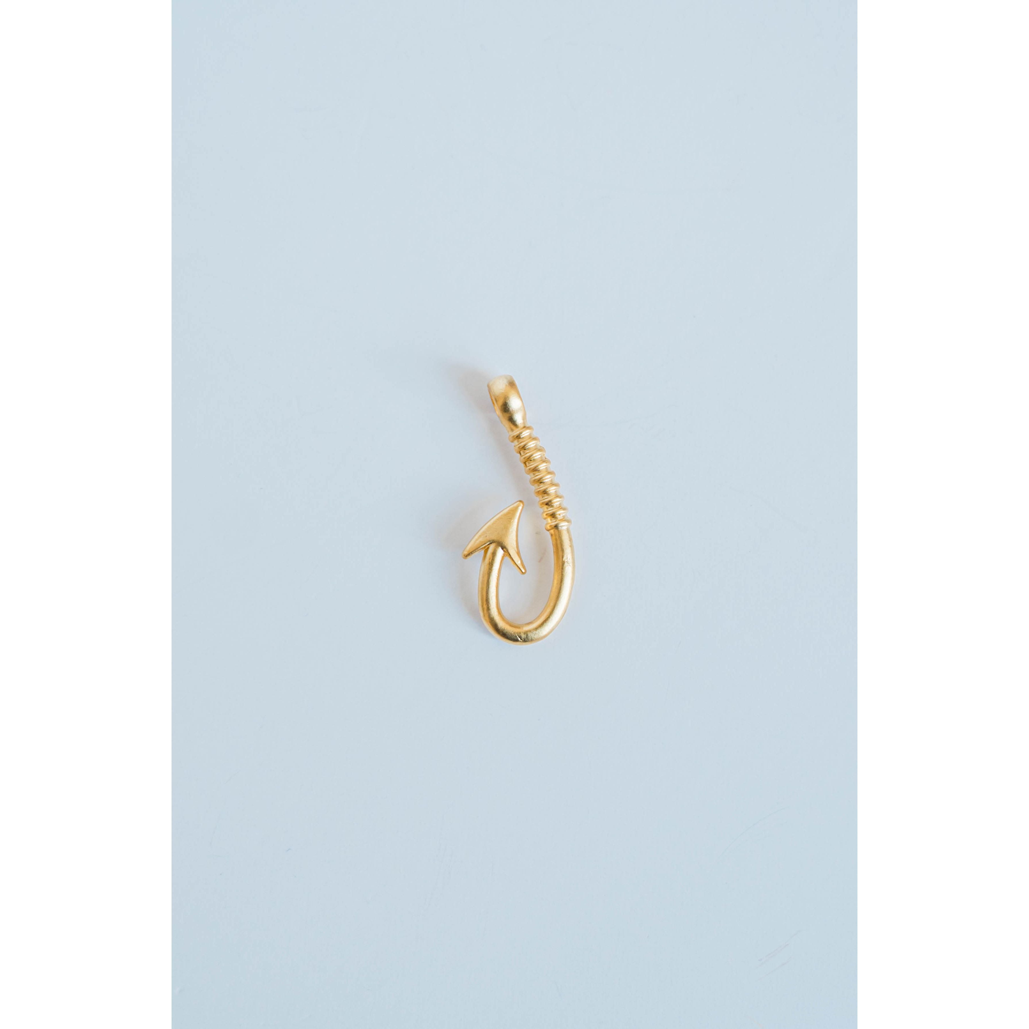 gold textured fishing hook charm on a light grey background