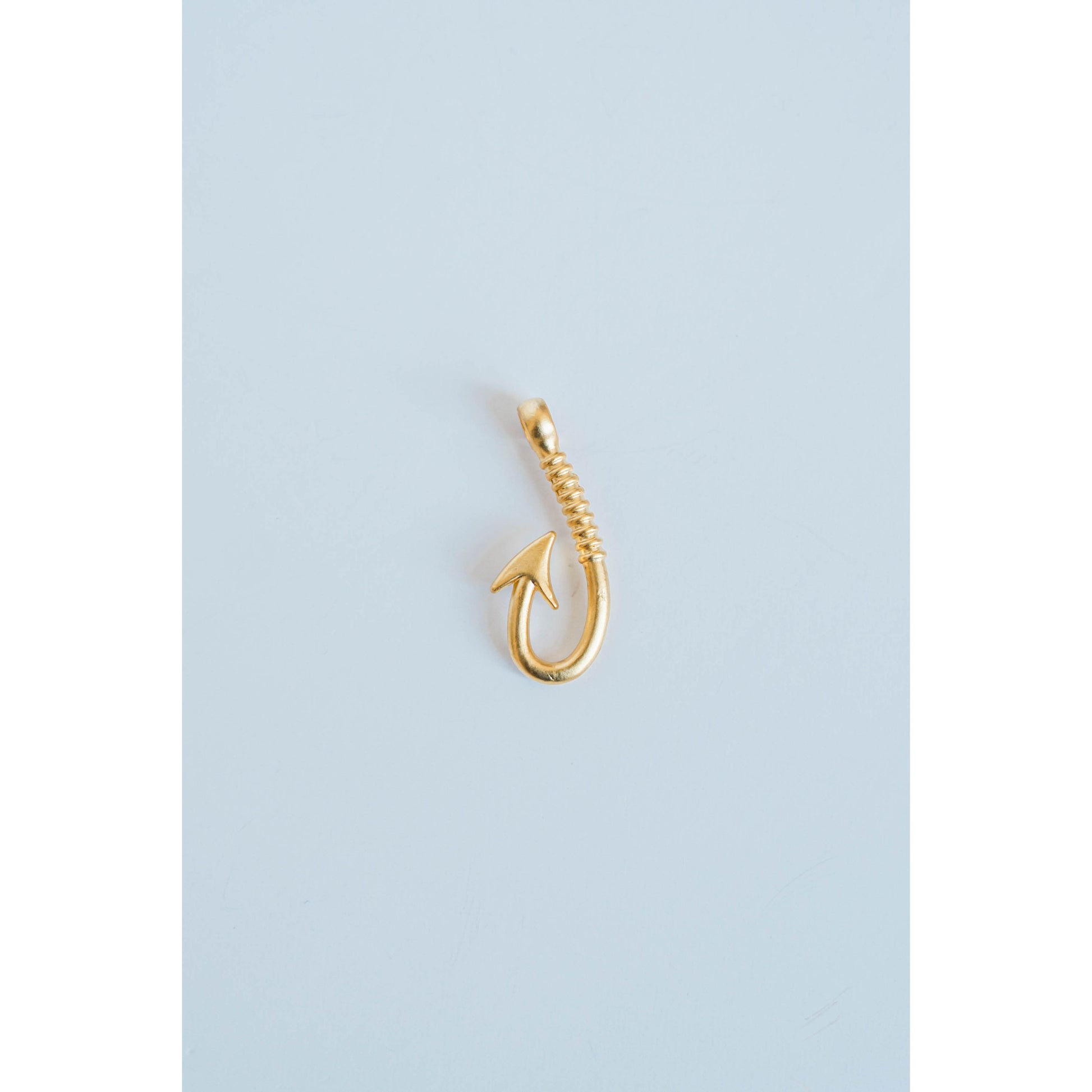 gold textured fishing hook charm on a light grey background