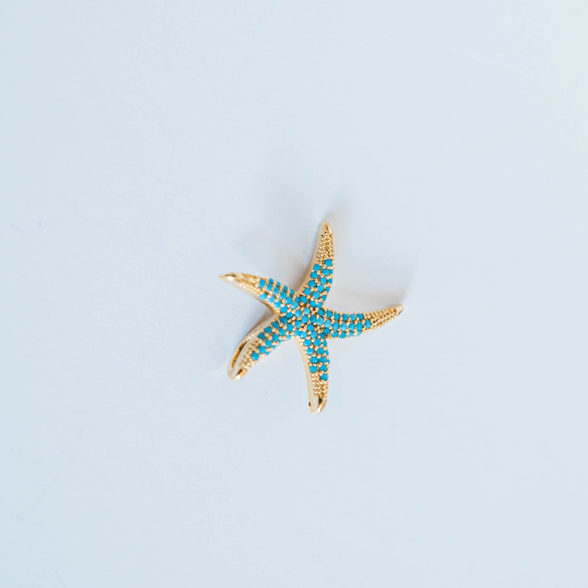 Starfish-shaped charm with turquoise stones on a light grey background
