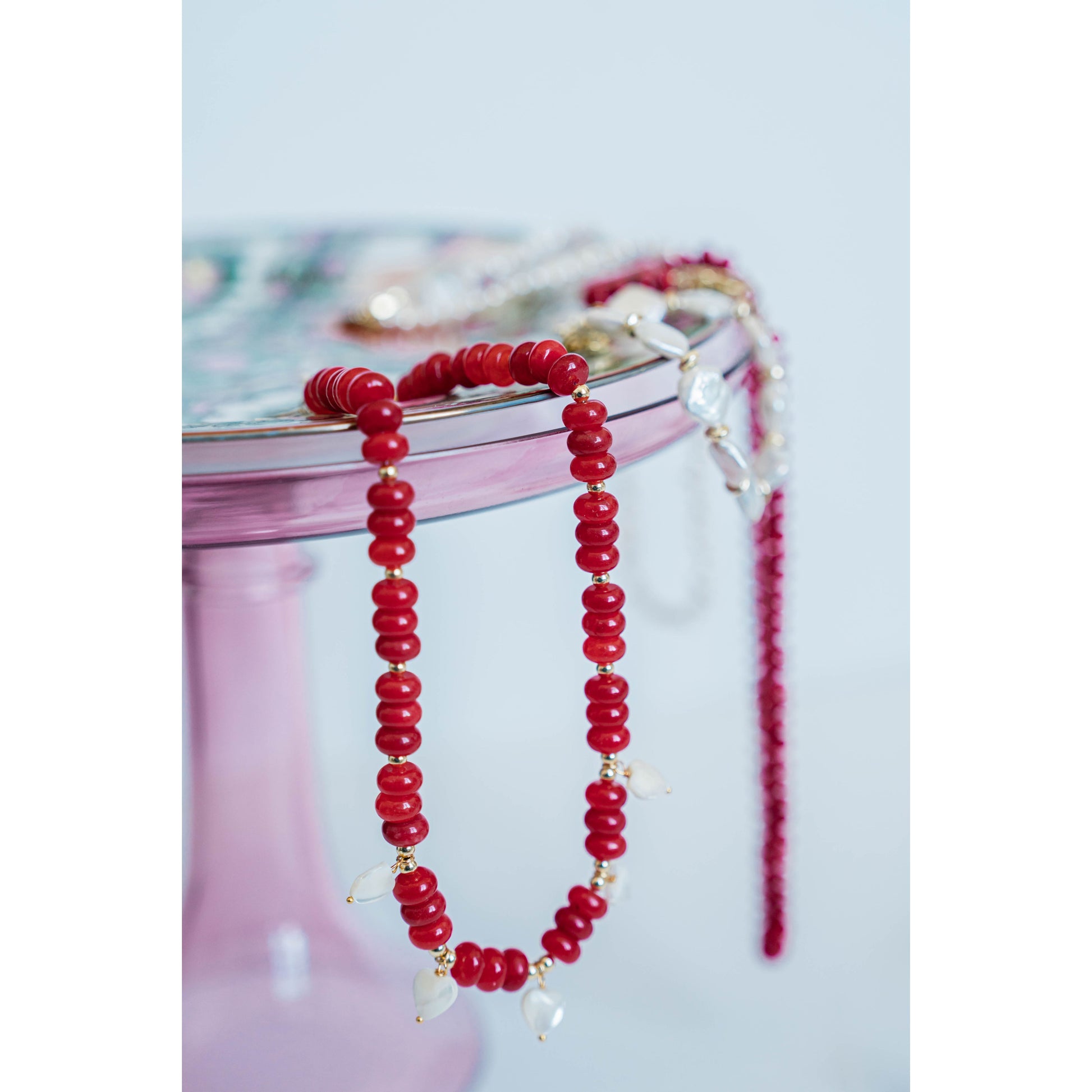 red beaded necklace with white pearl heart charms draped over a pretty cake stand